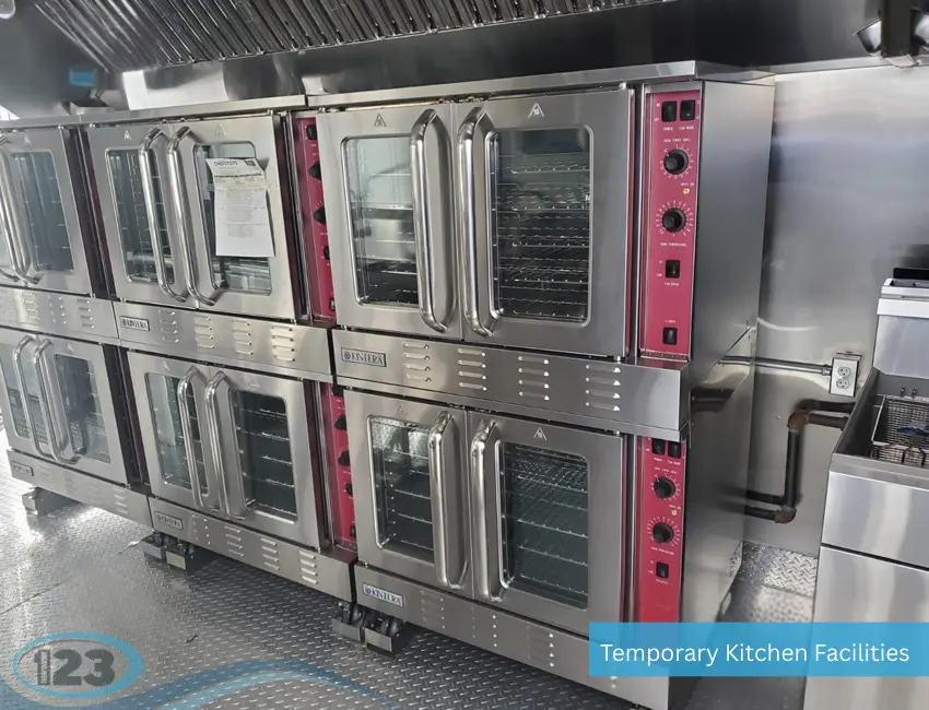 A row of stacked commercial stainless steel convection ovens with red control panels inside a temporary kitchen facility.