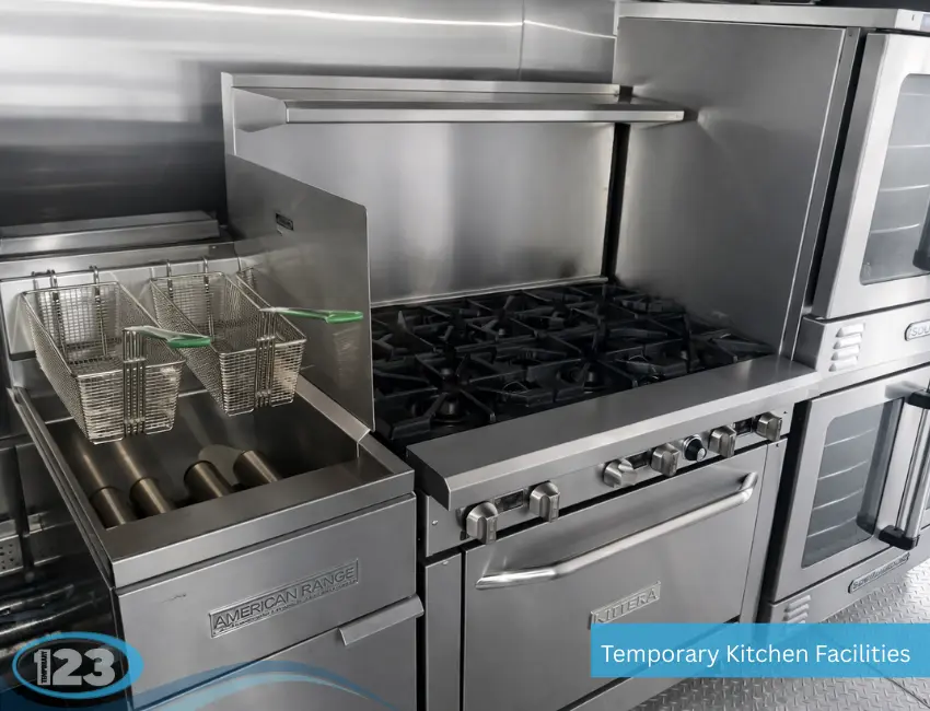 Commercial stainless steel cooking equipment inside a temporary kitchen facility, including a deep fryer with twin baskets next to a multi-burner stove and oven.