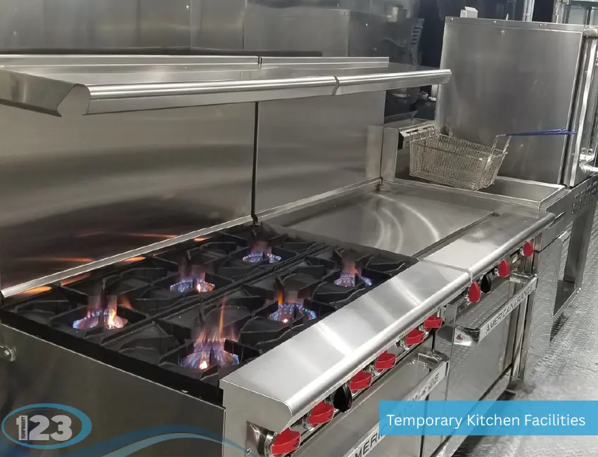 A professional stainless steel cooking line inside a temporary kitchen facility, showcasing lit gas burners on a commercial stove next to a flat-top griddle and a deep fryer.