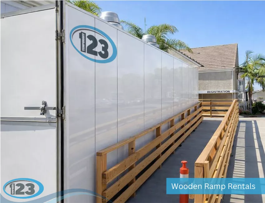 An exterior view of a long wooden accessibility ramp with handrails running alongside a white temporary mobile unit featuring "Temporary 123" branding.
